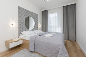 A minimalist bedroom with a gray padded bed, two bedside tables, and a large round mirror as the focal point above the headboard.