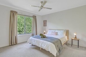 A master bedroom is well-lit and features a large window, bedside table, a ceiling fan and built-in wardrobes.
