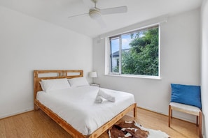 The bright second bedroom is clad in white with a queen-bed, side table and reading light.