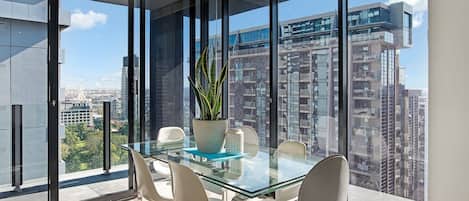 A glass dining table for six is framed by floor-to-ceiling windows offering  expansive views of the surrounds