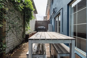 The spacious outdoor deck offers sunshine, a timber table for al fresco dining, and a lush grass area. Note that the BBQ has been removed.