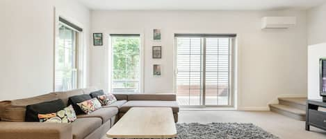 A downstairs living area provides an open plan space filled with natural light, and an L-shaped couch that faces a flat-screen TV with Foxtel