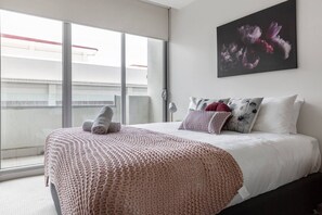 A large bedroom is furnished with a queen bed, built-in wardrobes with floor-to-ceiling mirrors and direct access to the balcony that overlooks the street