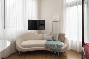 A stylish sofa and TV invite rest and relaxation, with large windows and floor-to-ceiling mirrors maximising natural light and creating a sense of spaciousness. 
