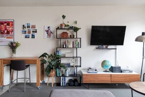 Step into the vibrant living area, a haven for the curious minds and creative souls. Movie frames, a record player, shelves of books, and a stylish workspace create an eclectic den of pop culture.