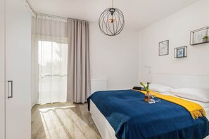 A cozy bedroom with a blue and yellow bedspread, white curtains, and minimalist design.

