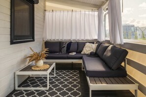 A covered terrace with comfortable seating and a black and white rug, offering a cozy spot to relax and enjoy the outdoors.
