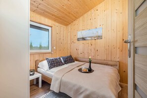 A compact bedroom with a wooden interior, a double bed, and minimalistic decor, emphasizing simplicity and comfort.
