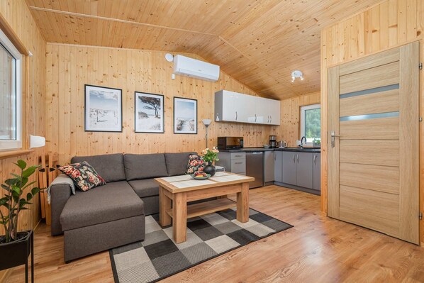 A cozy living space with wooden paneling, a gray sofa, a coffee table, and natural light streaming through the windows, creating a warm and inviting ambiance.
