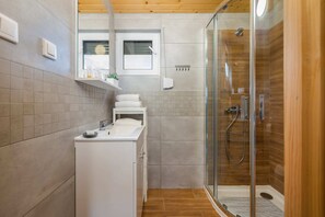 A bright bathroom with beige tiles, a walk-in shower, and a washing machine, combining functionality with modern design.
