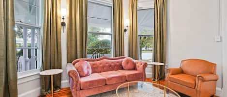 Living Room with Rose Couch, Arm Chair, Stylish Sconce LIghts and Floor to Ceiling Privacy Window Treatments