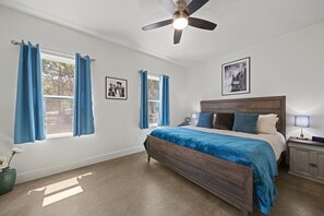 Bedroom with a bed, two ceiling fans, and a nightstand. The room is decorated in a simple and modern style, with white walls and light wood furniture.