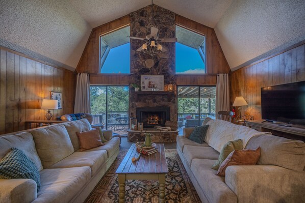 Open living space with a massive stone fireplace & access to a big outdoor deck.