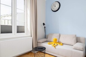 A bright seating area with a beige sofa, a small coffee table, and a window letting in natural light.
