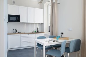 A compact kitchenette with white cabinets, a small dining table, and modern appliances, offering functionality.
