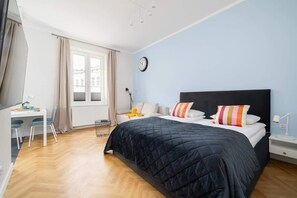 A spacious view of the studio, featuring a comfortable bed, a dining table, and cohesive decor.
