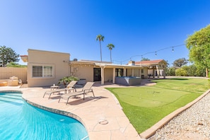 Spacious Entertainer's Backyard featuring a sparkling blue pool, hot tub, built-in BBQ, fire pit, lanai gazebo, putting green, half-court basketball, outdoor dining, and a large grass area perfect for yards games and furry friends.