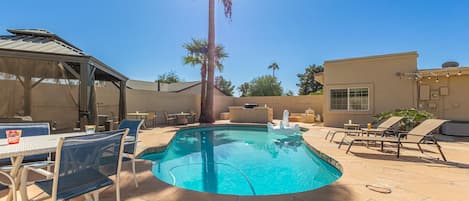 Spacious Entertainer's Backyard featuring a sparkling blue pool, hot tub, built-in BBQ, fire pit, lanai gazebo, putting green, half-court basketball, outdoor dining, and a large grass area perfect for yards games and furry friends.