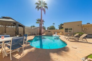 Spacious Entertainer's Backyard featuring a sparkling blue pool, hot tub, built-in BBQ, fire pit, lanai gazebo, putting green, half-court basketball, outdoor dining, and a large grass area perfect for yards games and furry friends.