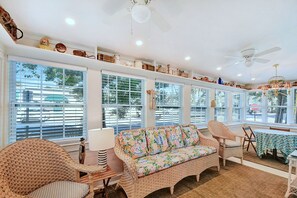 Bright Sunroom Lounge – The Stumble Home - Bask in the light-filled sunroom featuring wicker seating, recessed lighting, and walls of windows that bring the island sunshine indoors.