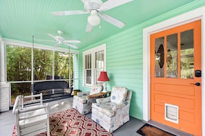Screened front porch with swing and orange door near East Beach - This East Beach gem welcomes you with a mint-green screened front porch, complete with a porch swing, floral armchairs, and overhead fans. The bold orange door adds personality and charm, setting the tone for a laid-back St. Simons Island stay just blocks from the sand.