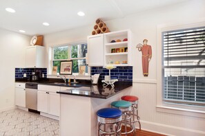 Colorful breakfast bar and navy tile kitchen at Mary’s House nea - Enjoy morning coffee or a quick bite at the retro-style breakfast bar at Mary’s House, just blocks from East Beach. This kitchen features navy subway tile, granite countertops, stainless steel appliances, and playful red and blue stools that bring vintage charm to the coastal vibe.