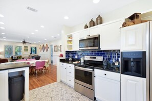 Open kitchen with navy tile backsplash and full view into dining - Mary’s House features a bright open kitchen with a navy subway tile backsplash, white cabinets, and stainless steel appliances. The view extends into the dining room and cozy living area, highlighting the home’s open-concept layout and family-friendly flow.