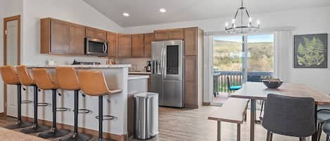 Fully-equipped kitchen with modern countertops, bar stools, a spacious dining table, and large windows that flood the space with natural light.