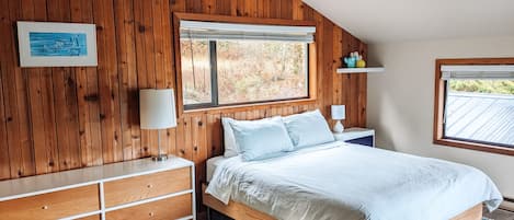 The master bedroom is large and filled with light and warm wood walls.