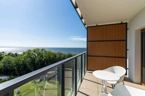 A balcony with a glass railing and a small table, overlooking lush greenery and providing a serene outdoor space.

