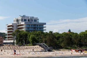 A view of a modern beachfront building with a sandy beach and trees, blending urban living with nature.
