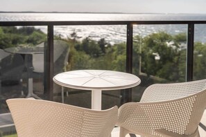 A balcony dining area with a round table and two chairs, surrounded by lush green scenery, perfect for outdoor meals.
