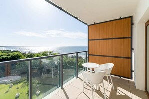 A balcony with a round table and chairs, offering a panoramic view of the surrounding greenery and coastline.
