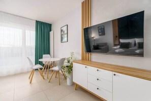 A modern living area featuring a wall-mounted TV, a wooden entertainment unit, and a large window with green curtains.
