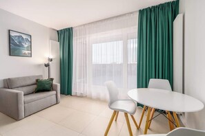 A cozy living and dining space with a gray sofa, a round table, and large windows, creating a bright and inviting ambiance.
