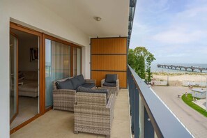 A balcony with rattan furniture, including a cozy seating area and a table, overlooking a scenic outdoor view.

