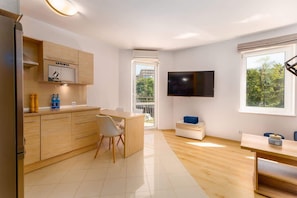 A compact living space featuring a small sofa, a TV, and natural light from a large window, perfect for relaxation.
