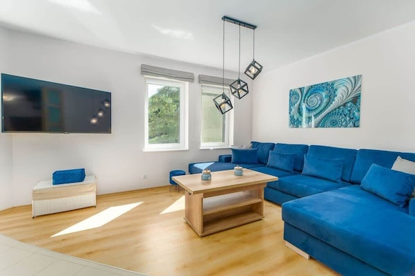 A bright living room with a modern blue sectional sofa, a mounted TV, and stylish décor, creating a cozy atmosphere.
