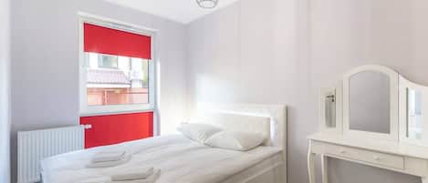 A bright bedroom with a single bed, a small desk, and a large window, creating a cozy and functional space.