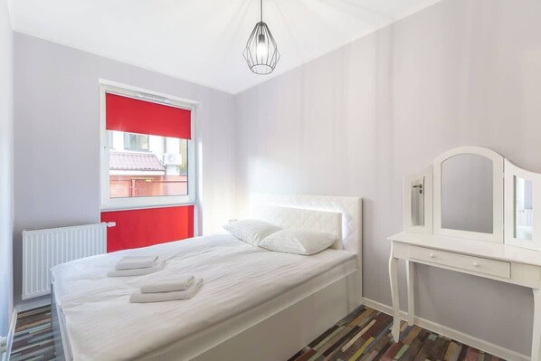 A bright bedroom with a single bed, a small desk, and a large window, creating a cozy and functional space.
