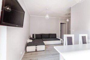 A modern living room with a comfortable gray sofa, a TV, and a dining table, designed for relaxation and practicality.
