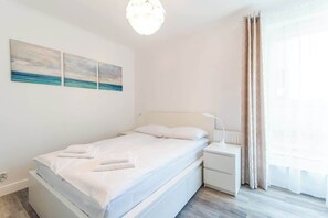 A bedroom with a double bed, white linens, and large windows with sheer curtains, offering a tranquil atmosphere.
