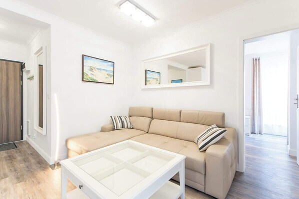 A bright living room with a beige sofa, a glass coffee table, and minimalist decor, creating a cozy and inviting space.
