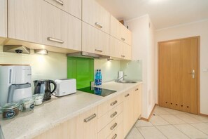 A compact kitchen with white cabinets, a green backsplash, and modern appliances.

