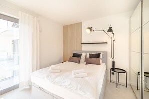 A cozy bedroom with a white bed, minimalist decor, and a mirrored wardrobe reflecting the space.
