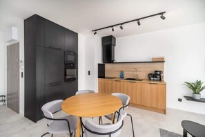 A small dining area with a wooden table and gray chairs, set next to a compact kitchen with modern finishes.
