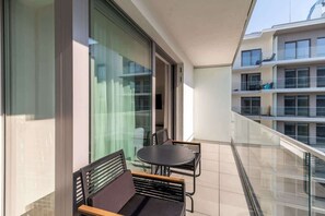 A balcony with black chairs and a small table, overlooking nearby buildings and greenery.

