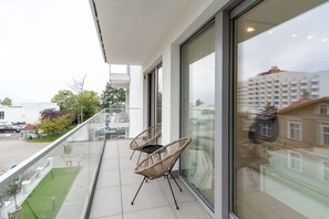 A balcony with modern chairs and a small table, overlooking a serene neighborhood.

