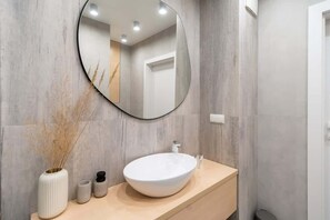 A stylish bathroom featuring a round mirror, a wooden vanity, and beige-toned walls.
