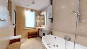 A bright bathroom with a corner bathtub, beige tiles, and a large window providing natural light.